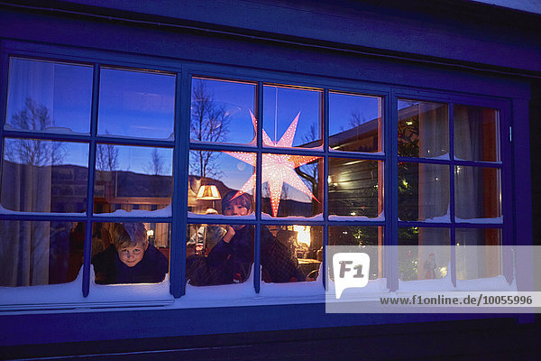 Two brothers looking out of cabin Christmas window at night