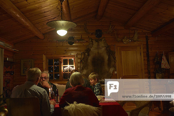 Three generation family sitting talking at Christmas table in log cabin at night