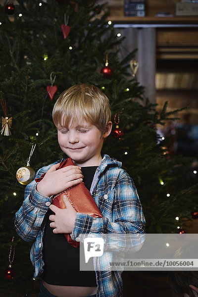 Junge hält Weihnachtsgeschenk mit geschlossenen Augen und Hoffnung