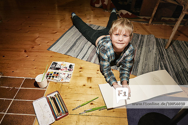 Junge auf dem Boden liegend mit Aquarellfarben und Skizzenblock
