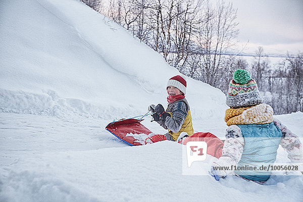 Zwei Brüder auf Schlitten auf schneebedecktem Hügel  Hemavan  Schweden