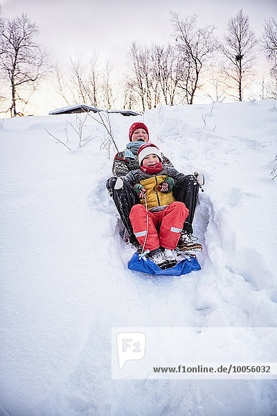 Two brothers playing on toboggan on snow covered hill  Hemavan Sweden