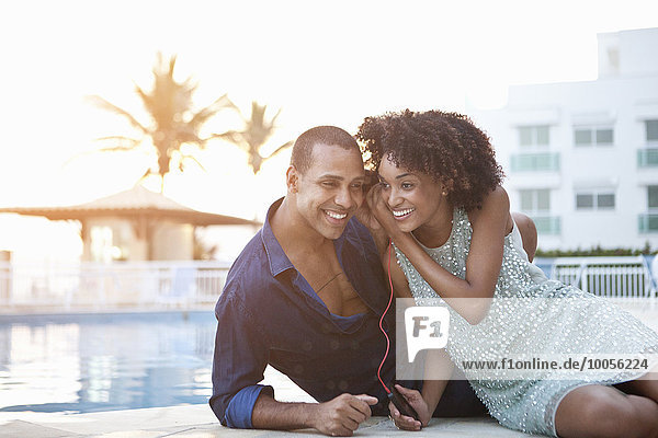 Stylish couple sharing earphones at poolside  Rio De Janeiro  Brazil