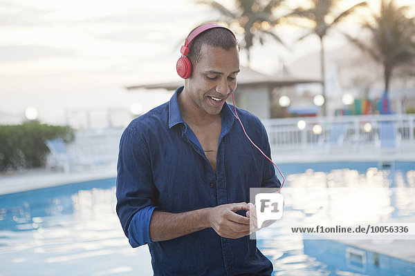 Mittlerer Erwachsener Mann  der Smartphone-Musik am Pool des Hotels  Rio De Janeiro  Brasilien  auswählt.