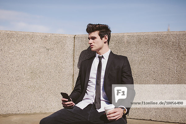 Enttäuschter junger Geschäftsmann auf dem Stadtsitz mit Smartphone