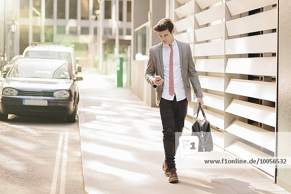 Ein junger Geschäftsmann liest Smartphone-Texte  während er außerhalb des Büros spazieren geht.