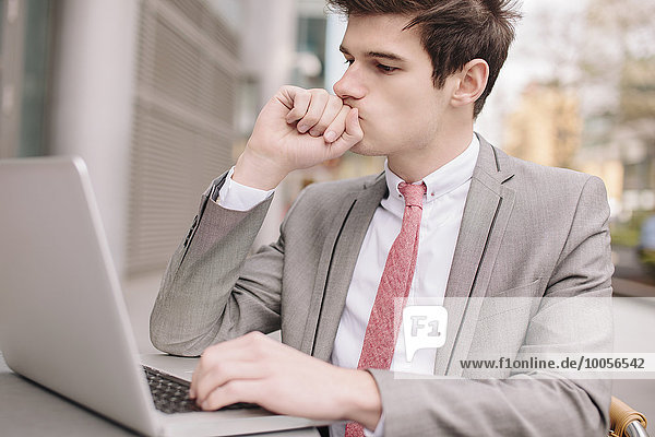 Worried young city businessman using laptop at sidewalk cafe