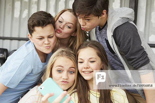 Five boys and girls making faces for smartphone selfie in shelter