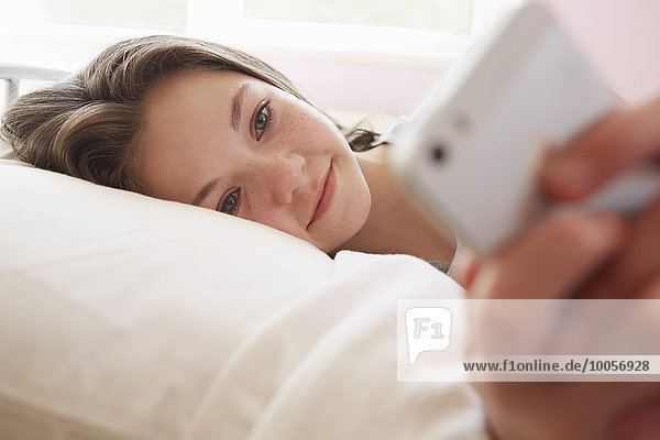 Mädchen auf dem Bett liegend SMS auf dem Smartphone