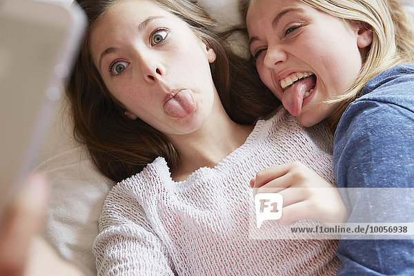Zwei Mädchen  die auf dem Bett liegen und Zungen für Smartphone Selfie herausstrecken.