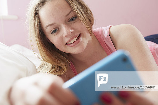 Mädchen liegt auf dem Bett und liest Textnachricht auf dem Smartphone.