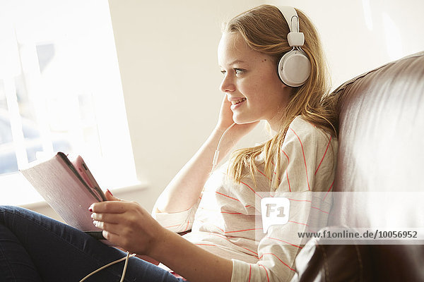 Mädchen auf dem Sofa trägt Kopfhörer und hört Musik vom digitalen Tablett.