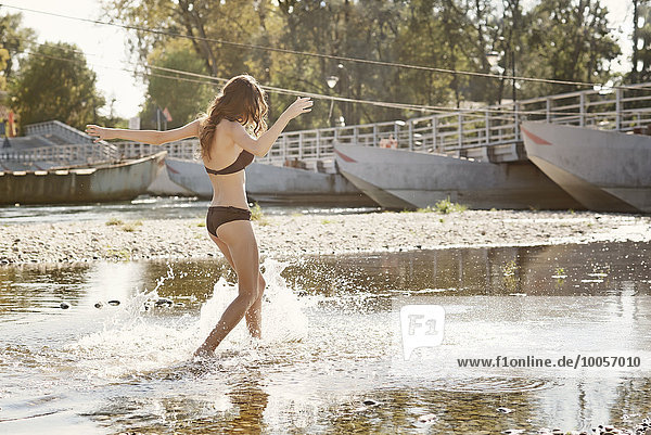Young woman wearing a bikini splashing and playing in river
