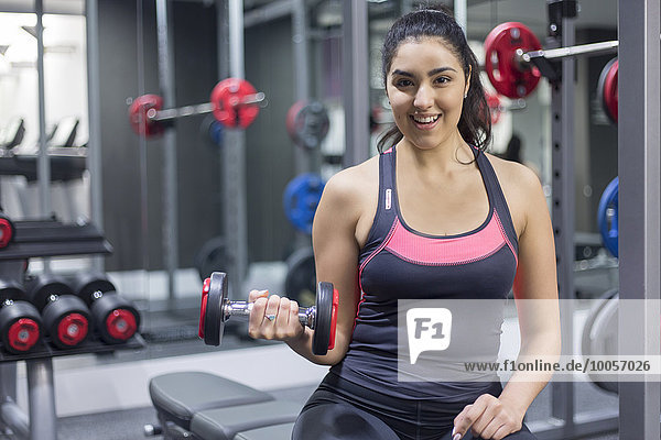 Portrait of a smiling young woman at gym holding dumbbell