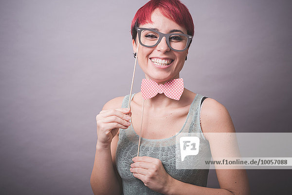 Atelierporträt einer verwirrten jungen Frau  die eine Brille vor dem Gesicht hält.