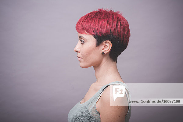 Profil Studioporträt einer jungen Frau mit kurzen rosa Haaren und Händen auf den Wangen