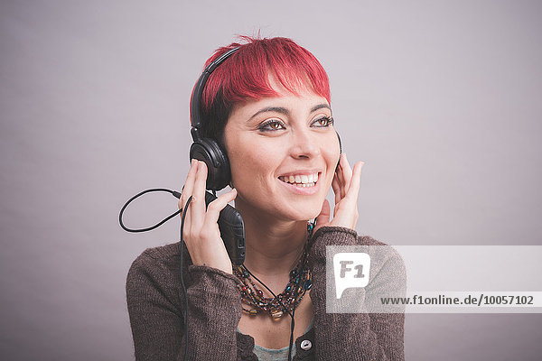 Studio-Porträt einer jungen Frau mit kurzen rosa Haaren,  die Kopfhörer hört.