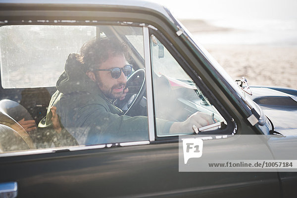 Man in parked vintage car lat beach fastening window