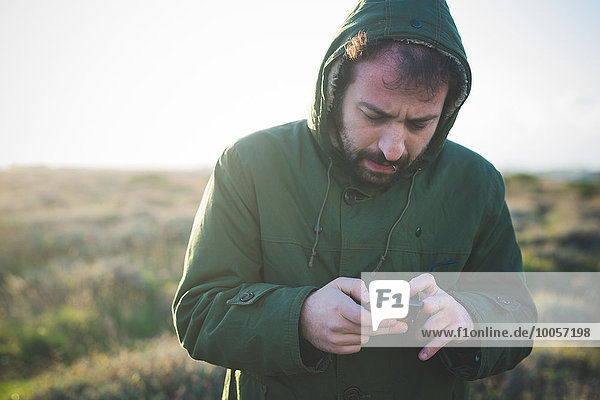 Mid adult man using smartphone whilst chewing matchstick in field