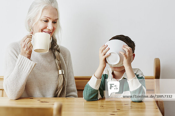 Junge trinkt Milch aus Schüssel mit Großmutter