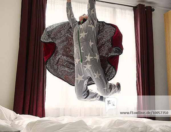 Junge mit Umhang auf dem Bett springend