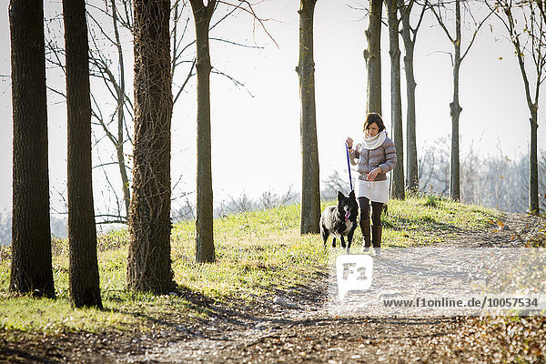 Mittlere erwachsene Frau  die mit ihrem Hund auf einem Feldweg spazieren geht.
