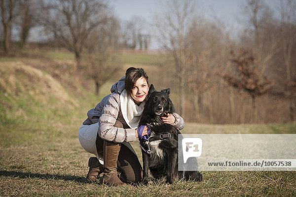 Porträt einer mittleren erwachsenen Frau  die mit ihrem Hund auf dem Feld kniend steht