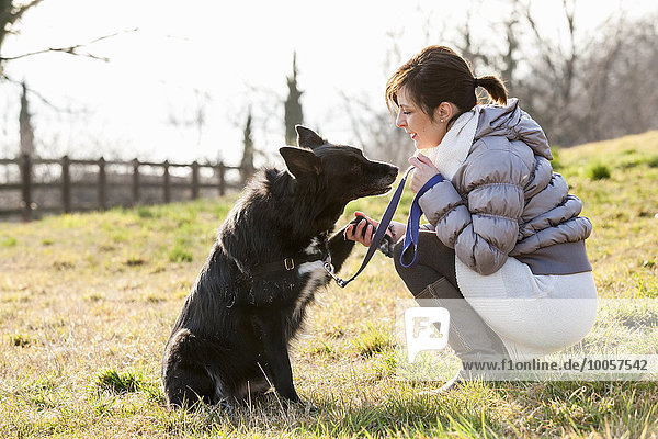 Mid adult woman training her dog to hold up paw in field