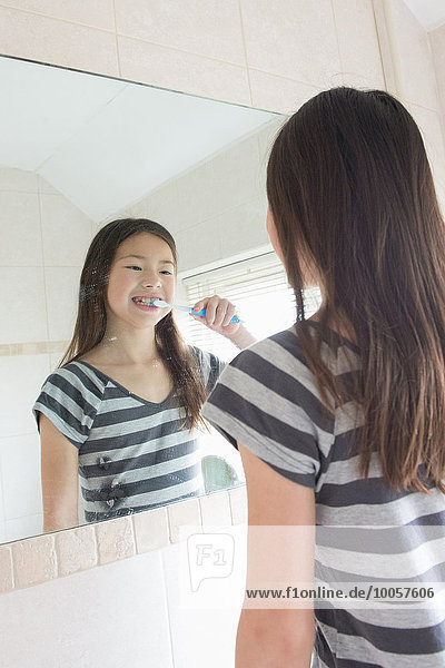 Girl brushing her teeth in bathroom mirror