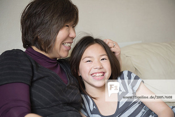 Smiling girl and her mother sitting on sofa