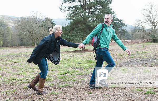 Hiking couple holding hands and running in field