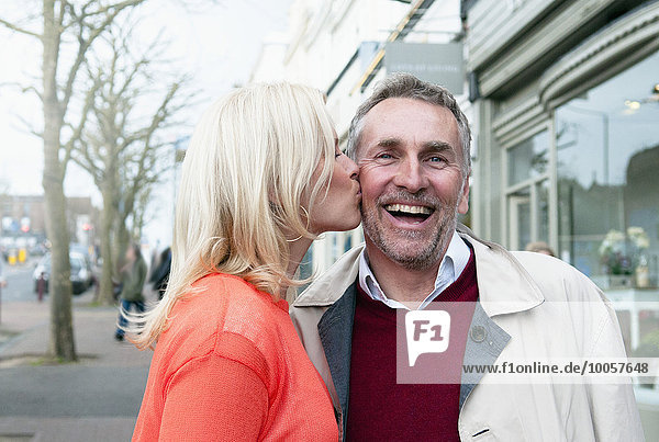 Woman kissing boyfriend on cheek on village street