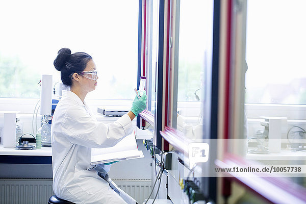 Junge Wissenschaftlerin mit Notizbuch beim Betrachten der Probe im Labor