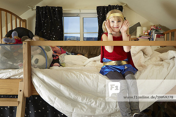 Porträt eines jungen Mädchens  das auf dem Bett sitzt und ein Kostüm trägt.