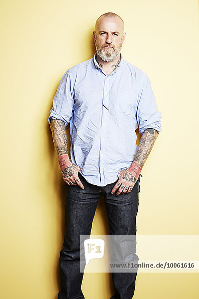 Reifer Mann mit Tattoos an Armen und Hals  gelber Hintergrund