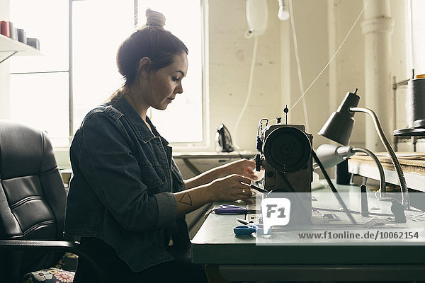 Young female seamstress using sewing machine in fashion studio