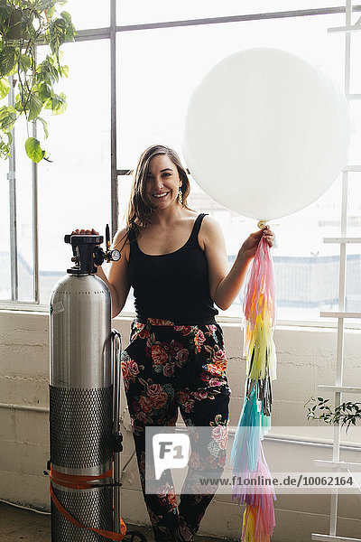 Porträt einer jungen Frau  die einen Heliumballon im Designstudio hochhält