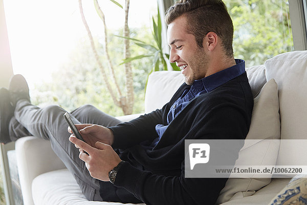 Porträt eines Mannes  der sich auf dem Sofa entspannt und mit den Füßen nach oben auf das digitale Lesegerät schaut.