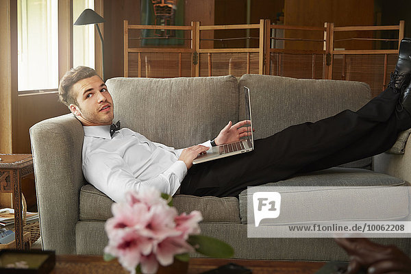 Porträt eines Mannes in schicker Kleidung auf dem Sofa liegend mit Laptop
