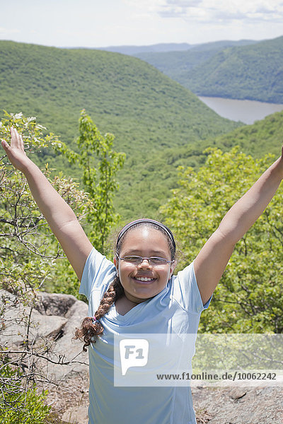 Young girl at top of hilly landscape  arms raised  smiling