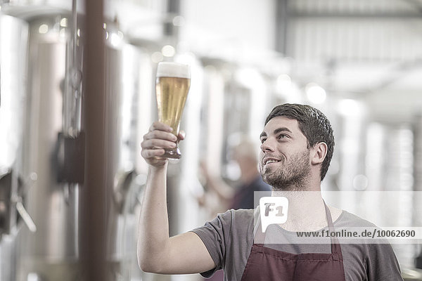 Brewer in brewery holding up a glass of beer