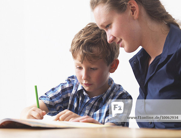 A six year old boy doing his homework with his mum at home