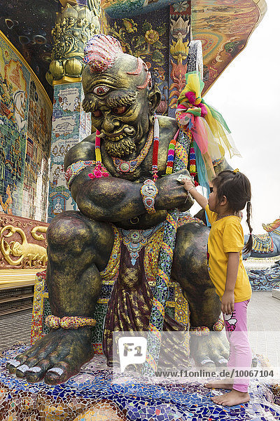 Mädchen reibt Geldschein an einer Yaksa Statue  Yak  Elefanten-Tempel Thep Wittayakhom Vihara  Wittayakom  Wat Baan Rai  Korat  Nakhon Ratchasima Provinz  Isaan  Isan  Thailand  Asien