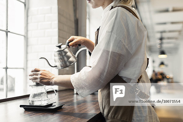 Seitenansicht Mittelteil des weiblichen Barista  der kochendes Wasser in den Kaffeefilter am Kaffeetresen gießt