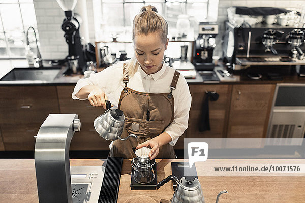 Hochwinkelansicht des weiblichen Barista  der kochendes Wasser in den Kaffeefilter an der Kaffeetheke gießt