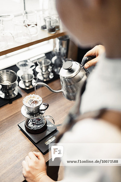 Hochwinkliges Bild von Barista  der kochendes Wasser in den Kaffeefilter am Tresen gießt.