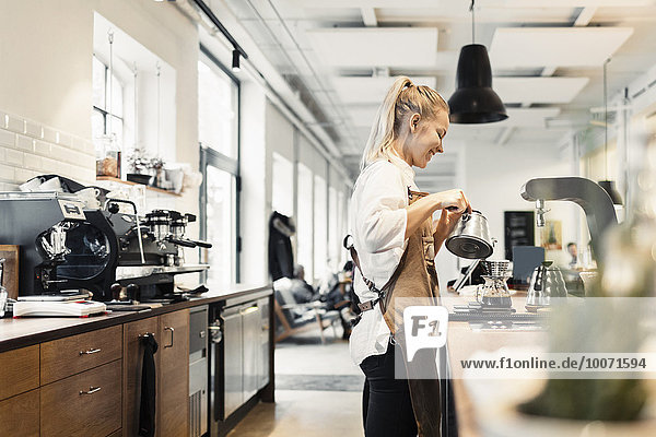 Side view of female barista preparing coffee at counter