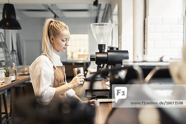 Female barista holding container by coffee maker at counter in cafe