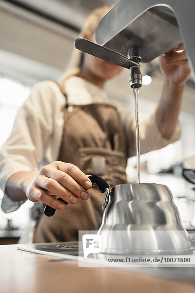 Weibliche Barista gießt kochendes Wasser in Kaffeekanne aus der Maschine an der Theke im Café
