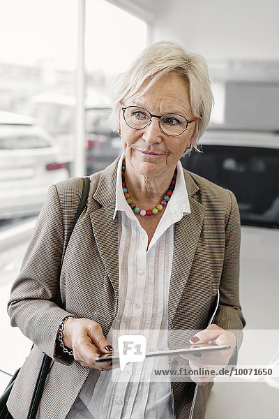 Senior Geschäftsfrau mit digitalem Tablett stehend im Autohaus